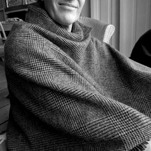 Black and white portrait of a model wearing the B108 Design Bulgarian wool plaid cape wrapped comfortably around the neck and shoulders.