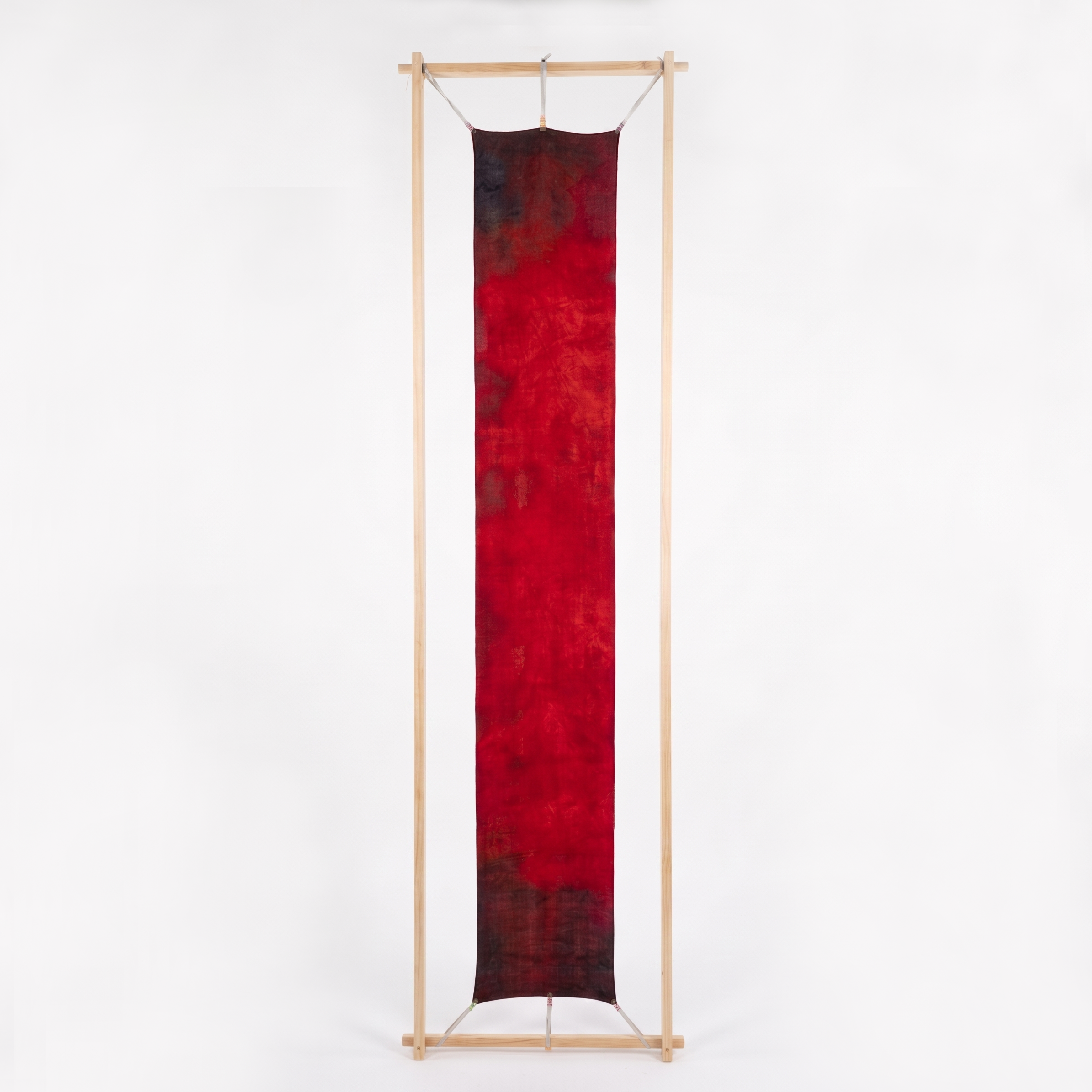 Ember Wool-Silk Scarf (Resonant Bloom Edition) stretched on a vertical timber frame against a white background, showing the full 30x180cm artwork in crimson, maroon and charcoal.