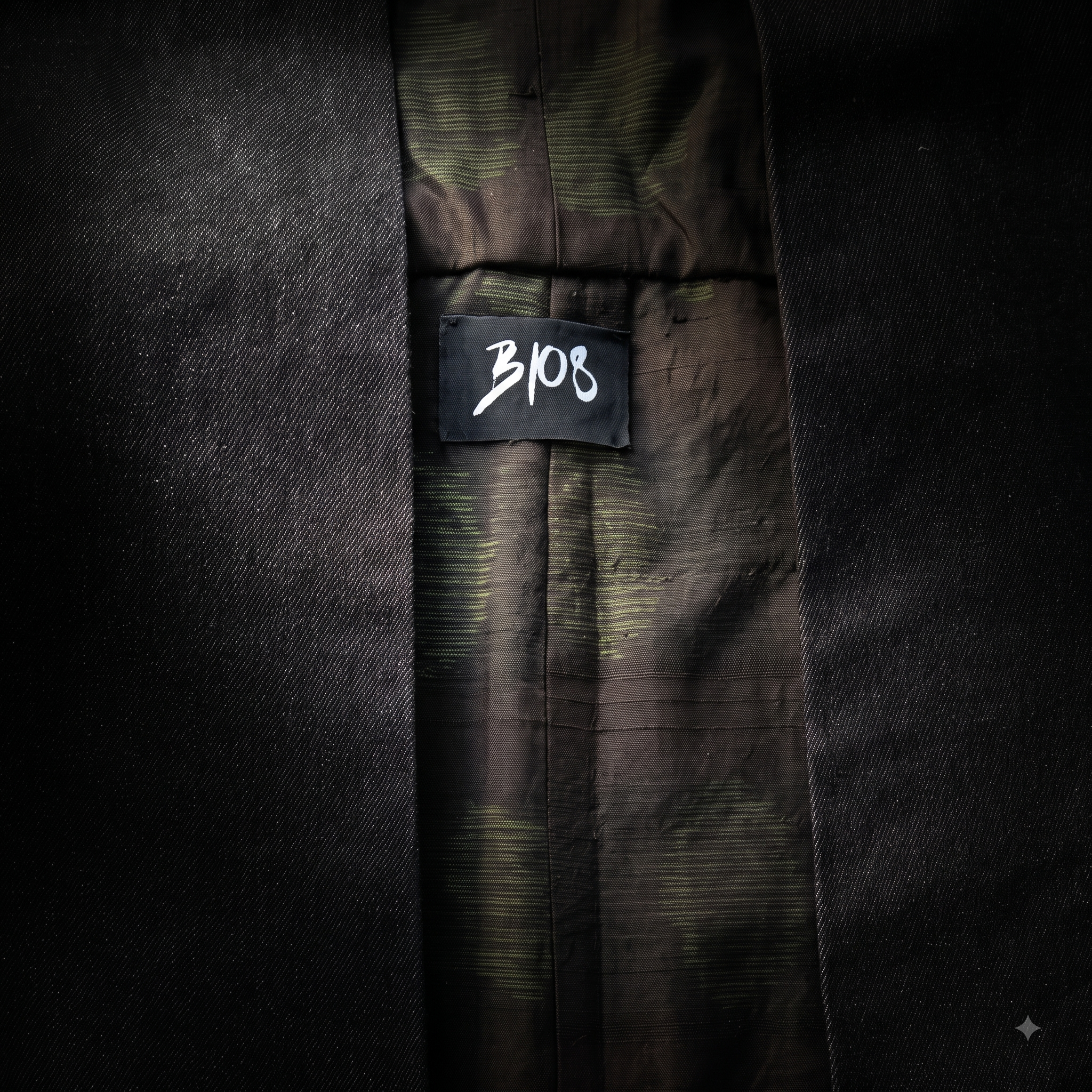 Macro detail shot of the B108 woven studio label attached to the patterned upcycled silk lining inside the black denim kimono vest.