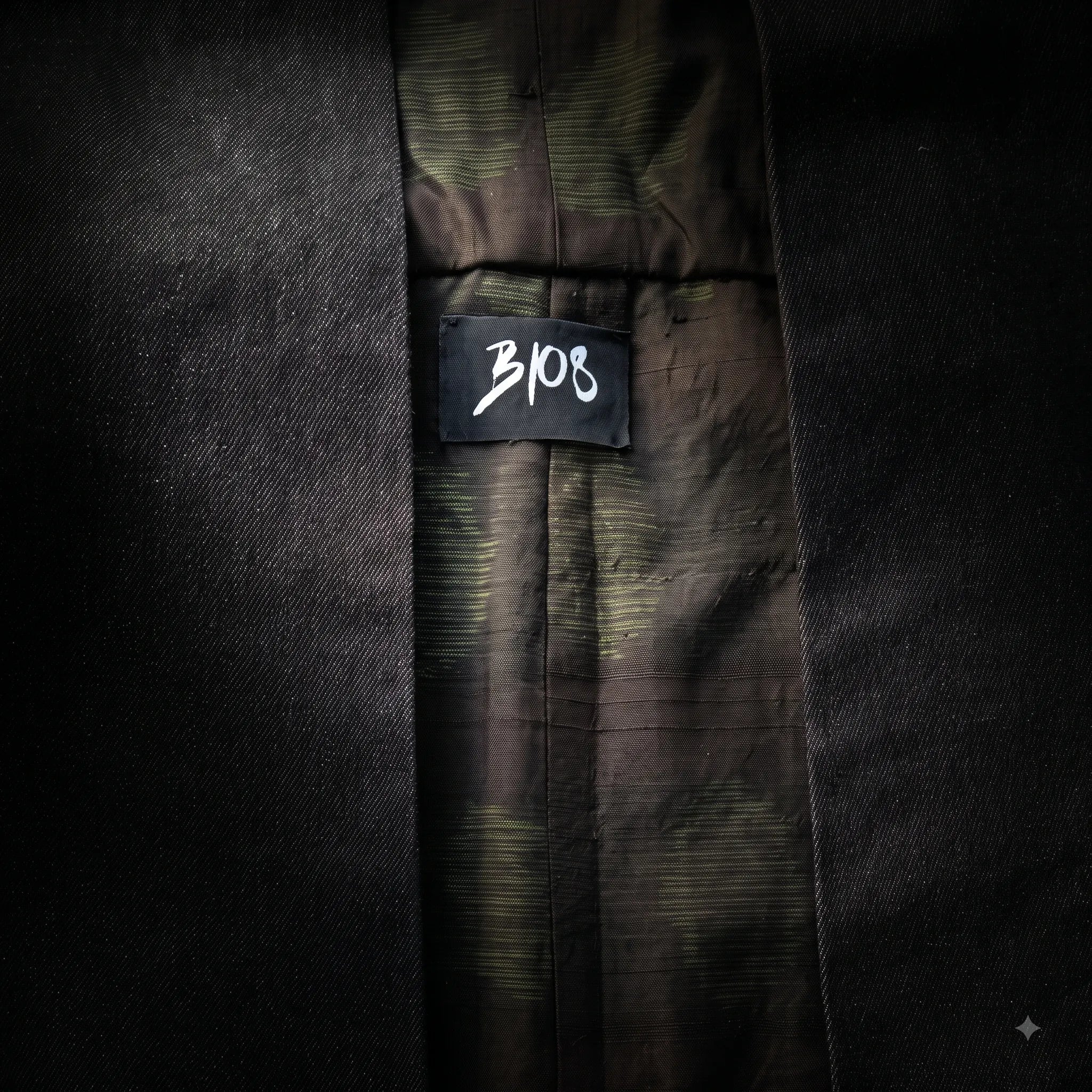 Macro texture detail of the Black Denim Kimono Vest revealing the inner black cotton denim weave, olive green patterned vintage silk lining, and stitched black B108 studio brand label by B108 DESIGN.
