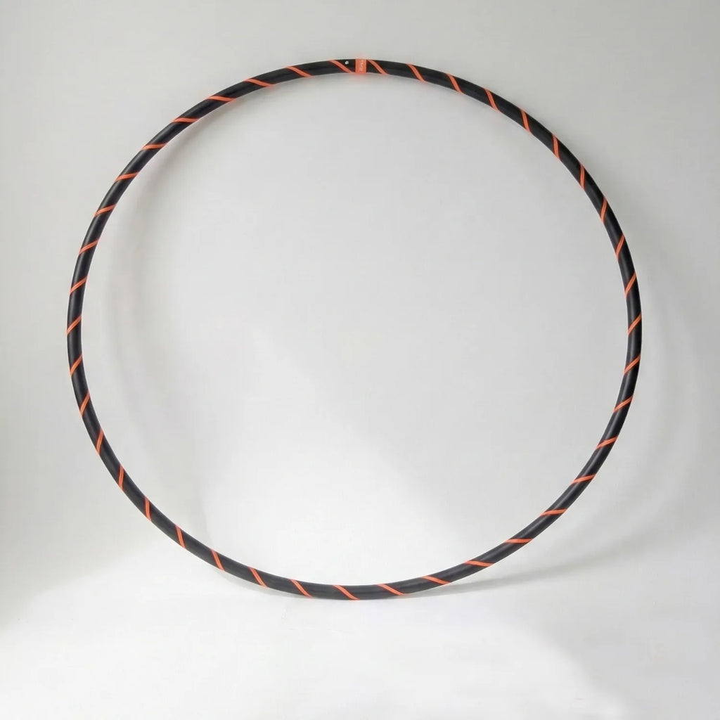 Studio shot of the B108 DESIGN Archival Dance Hoop in Electric Tiger featuring a fluoro orange and black spiral grip tape pattern against a white backdrop.