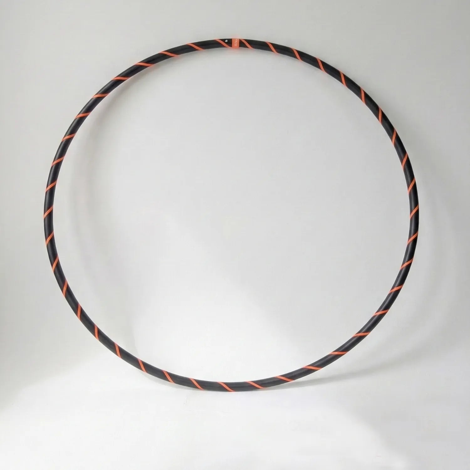 Studio shot of the B108 DESIGN Archival Dance Hoop in Electric Tiger featuring a fluoro orange and black spiral grip tape pattern against a white backdrop.