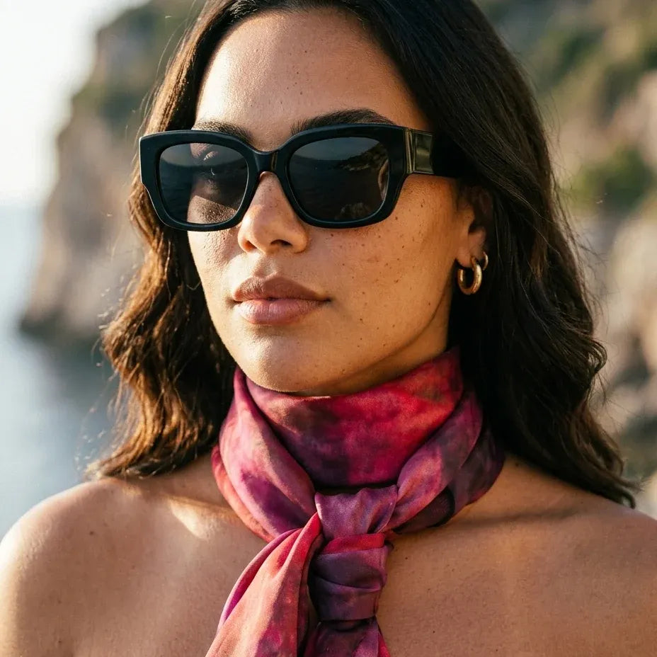 Outdoor portrait of a model wearing black sunglasses and the Ember luxury silk Habotai scarf by B108 Design tied around the neck, featuring a hand-dyed magenta and plum gradient.