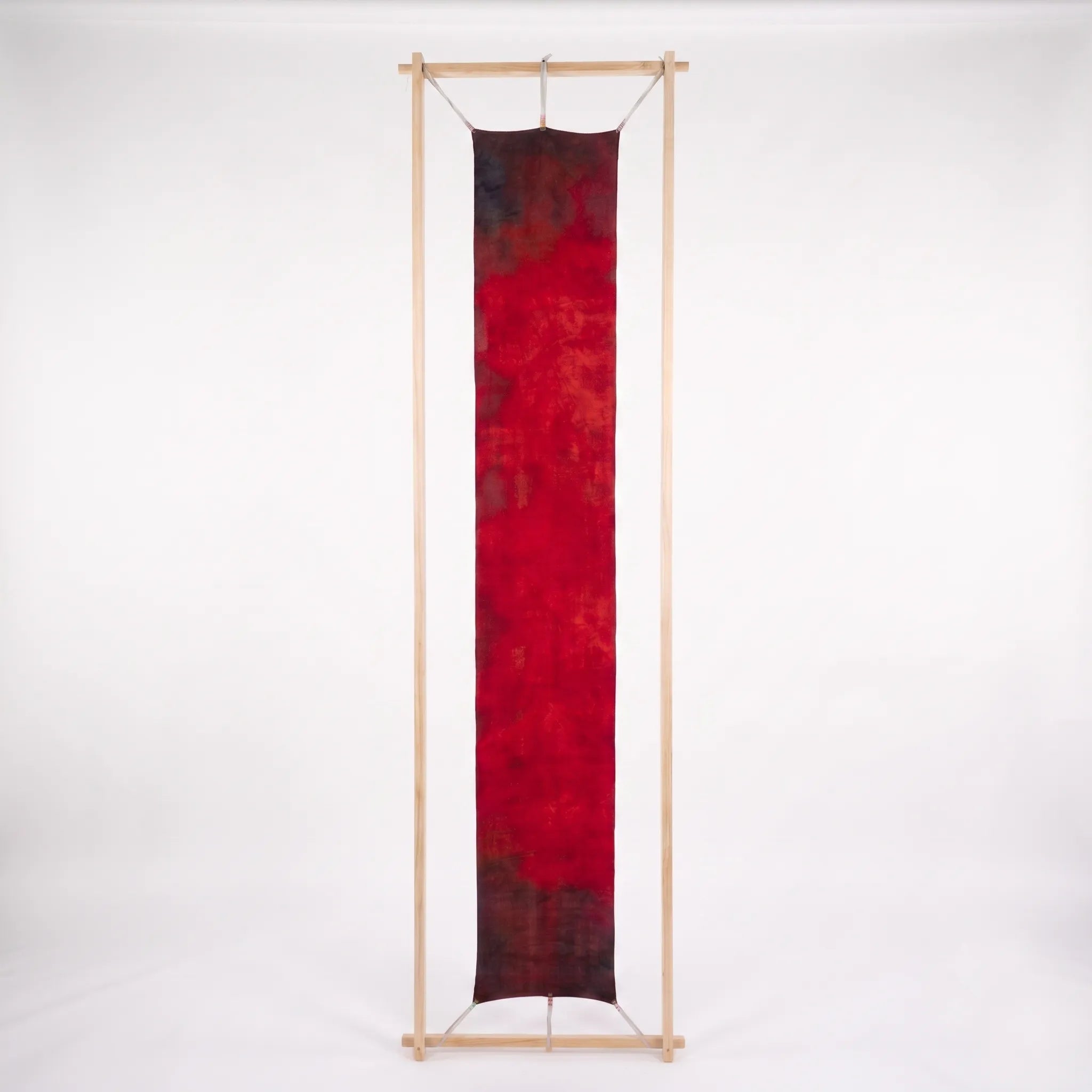 Full view of the Ember luxury silk-wool scarf by B108 Design displayed flat within a tall wooden frame, showing the complete hand-dyed crimson red gradient with dark charcoal edges.