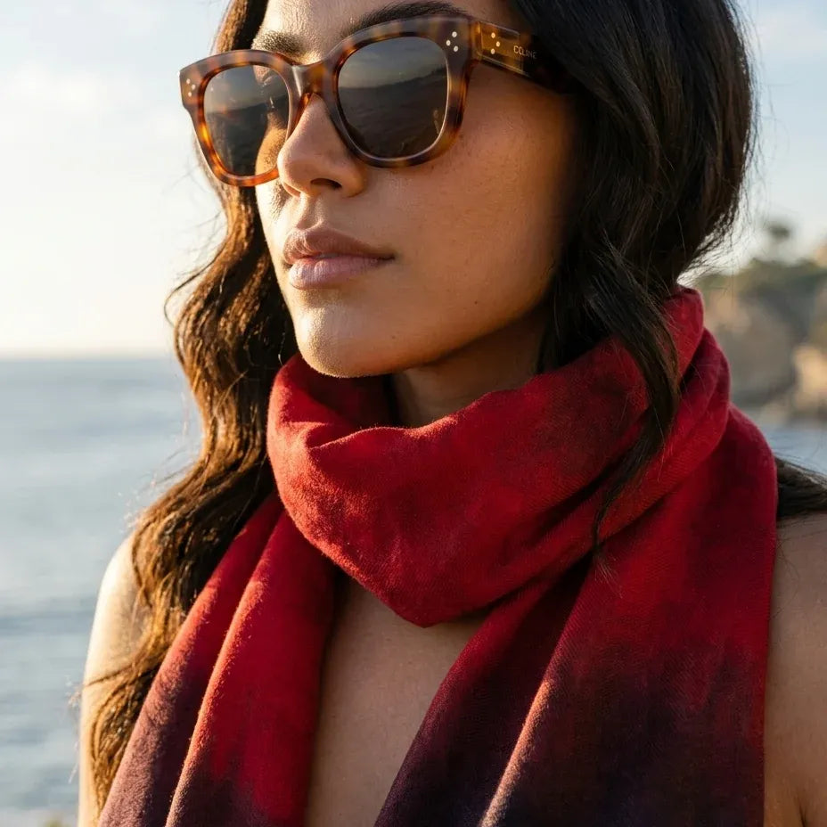 Outdoor lifestyle portrait of a model wearing tortoiseshell sunglasses and the Ember luxury silk-wool scarf by B108 Design in a crimson red gradient.