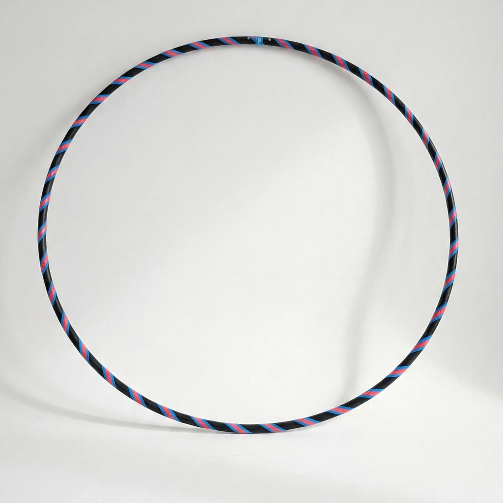 Studio shot of the B108 DESIGN Archive Glam Dance Hula Hoop in Cosmic Pulse, featuring a blue, pink, and black striped grip tape pattern against a white background. 