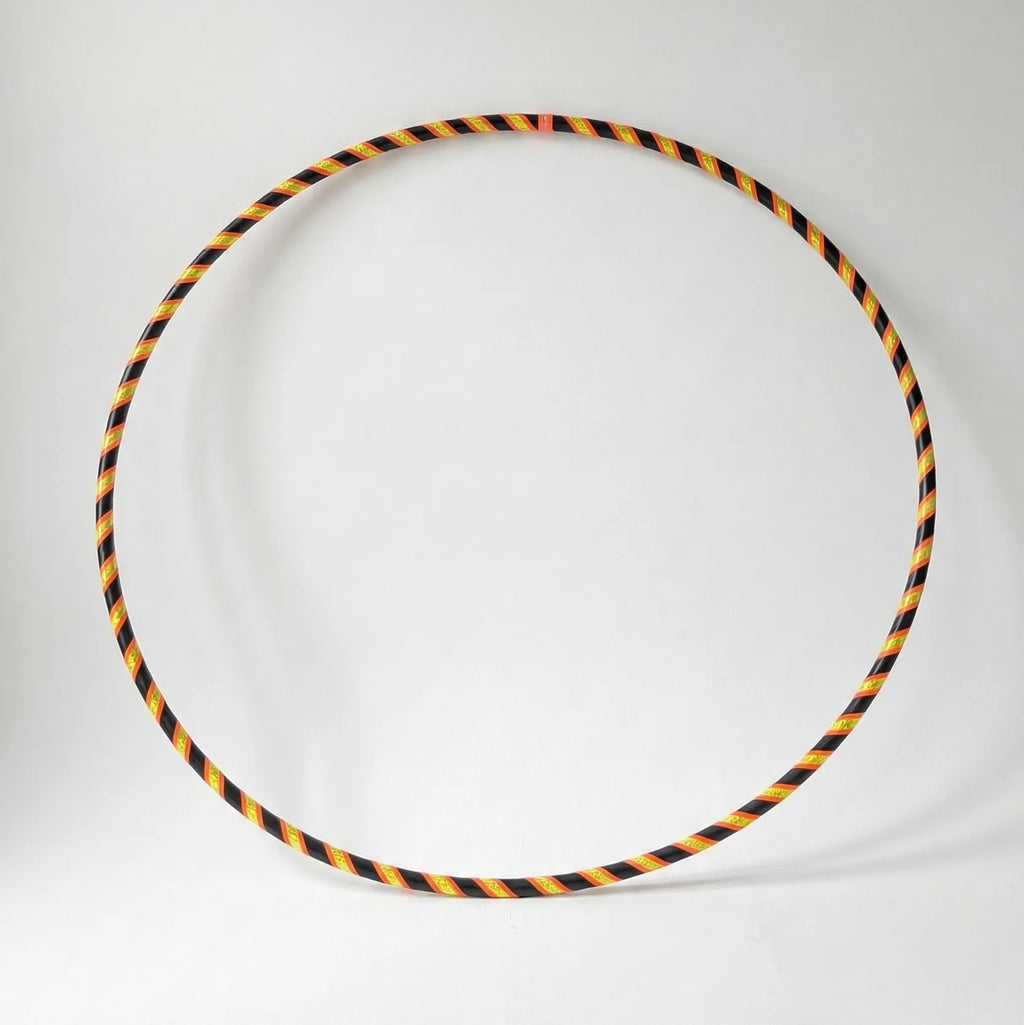 Studio shot of the B108 DESIGN Archive Glam Dance Hula Hoop in Techno Beetle, featuring a neon yellow, orange, and black spiral grip tape pattern against a clean white backdrop.