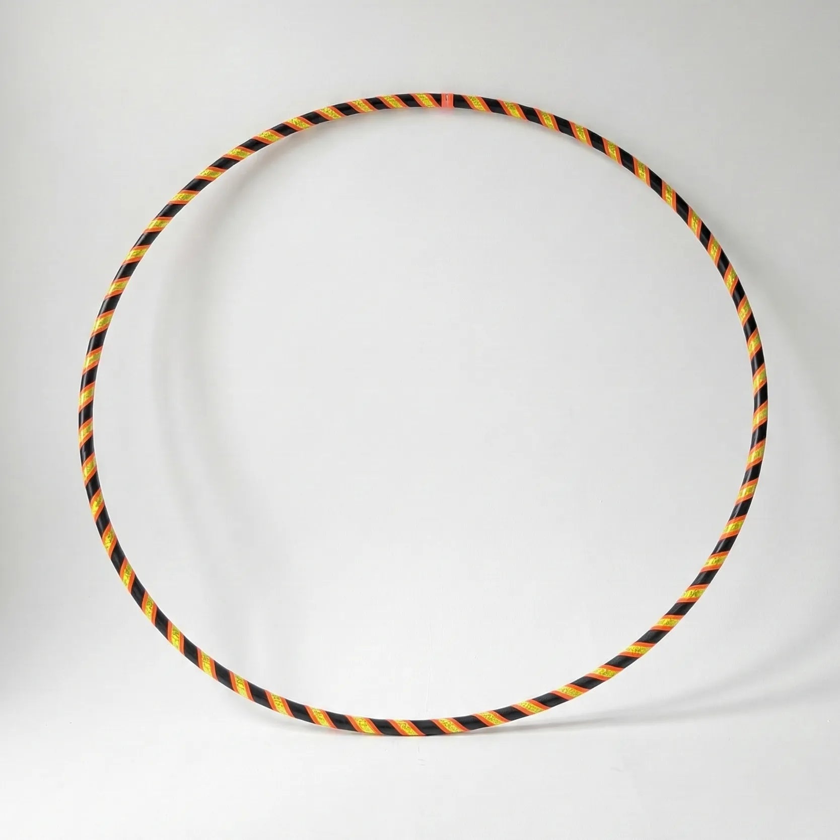 Studio shot of the B108 DESIGN Archive Glam Dance Hula Hoop in Techno Beetle, featuring a neon yellow, orange, and black spiral grip tape pattern against a clean white backdrop.