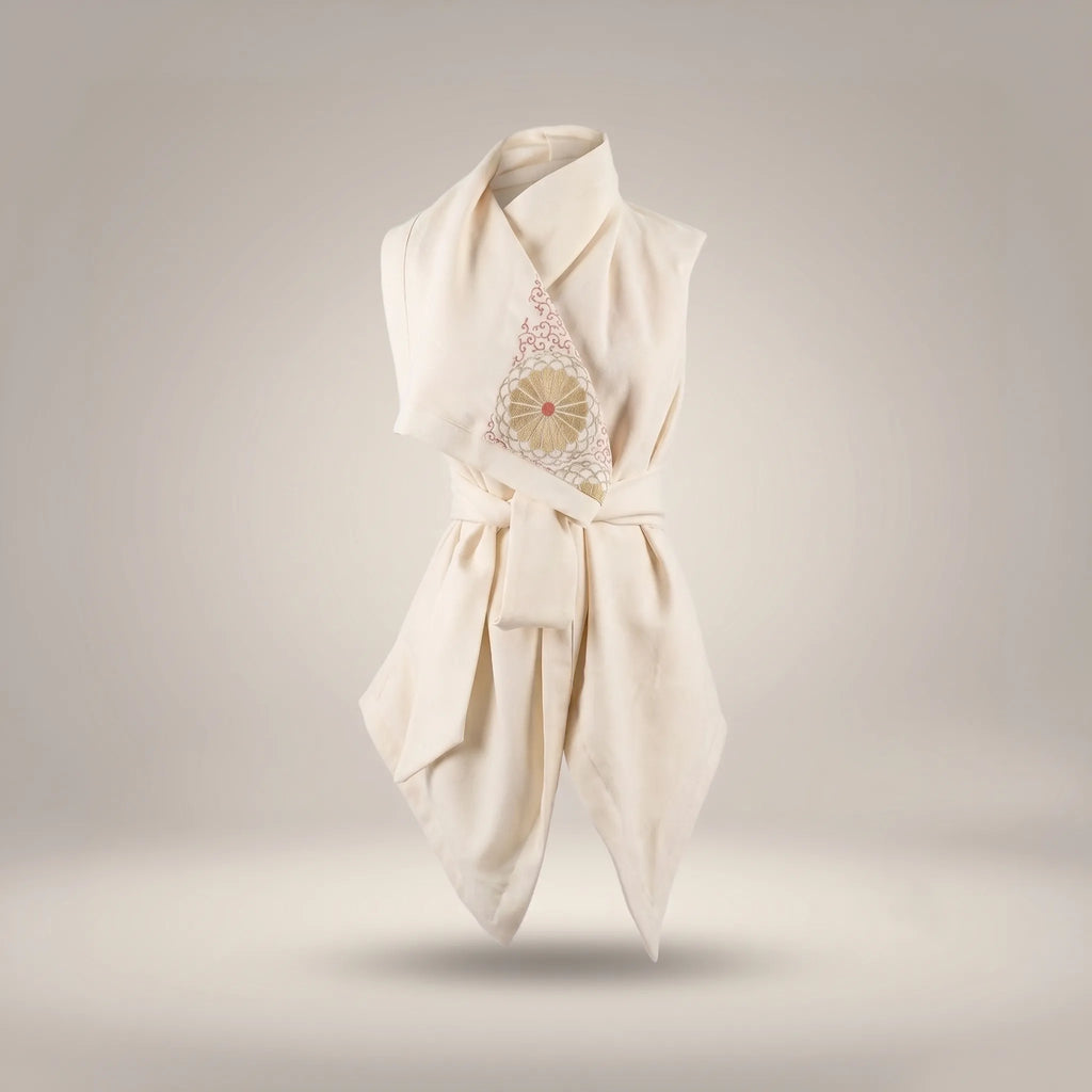 A high-angle view of the Merino Wool Kimono Vest in un-dyed cream wool, showing the sculptural wrapped tie-waist, cowl collar, and intricate gold and coral vintage Japanese silk motif detail, against a light grey background by B108 DESIGN.