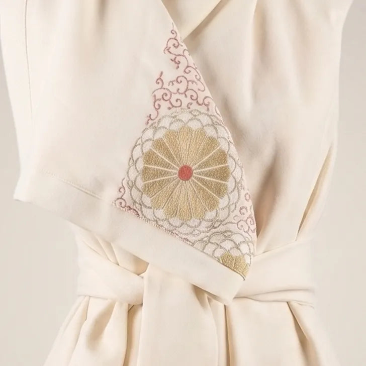 Close-up detail of the Merino Wool Kimono Vest in cream, highlighting the draped lapel with an embroidered gold and dusty rose vintage Japanese silk motif above a tied sash waist by B108 DESIGN.