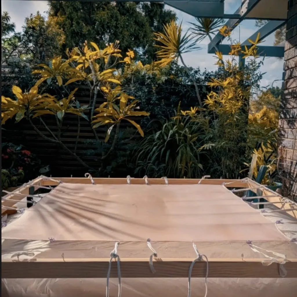 Natural silk fabric suspended on a traditional wooden stretching frame with cord ties in an outdoor garden studio setting by B108 DESIGN.