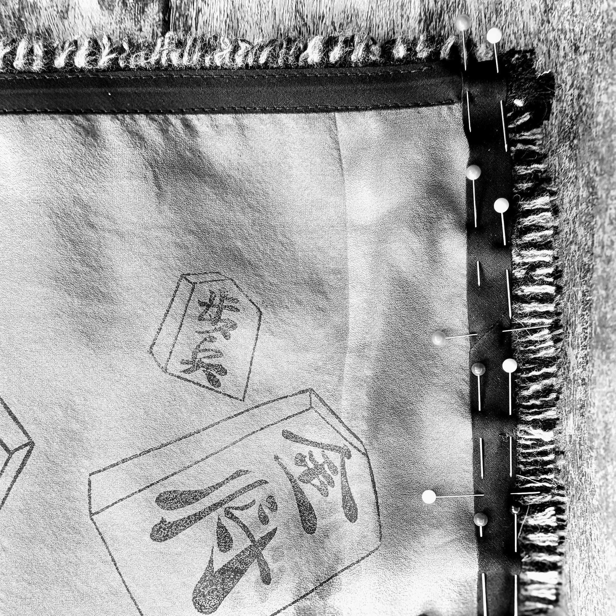 Behind-the-scenes detail of B108 Design artisan craftsmanship, showing printed silk lining fabric pinned along a woven fringe border with Japanese kanji motifs.