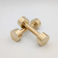 Studio shot of a pair of solid brass hand weights by B108 Design crossed over each other on a white background, displaying a brushed metallic finish