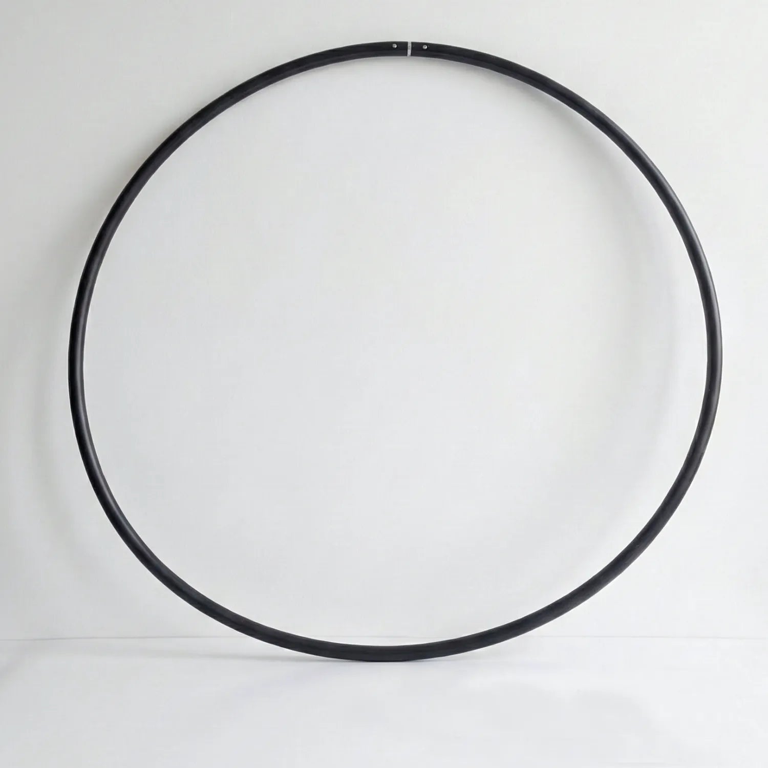 Studio shot of the B108 DESIGN weighted fitness hula hoop in obsidian black leaning against a white wall.