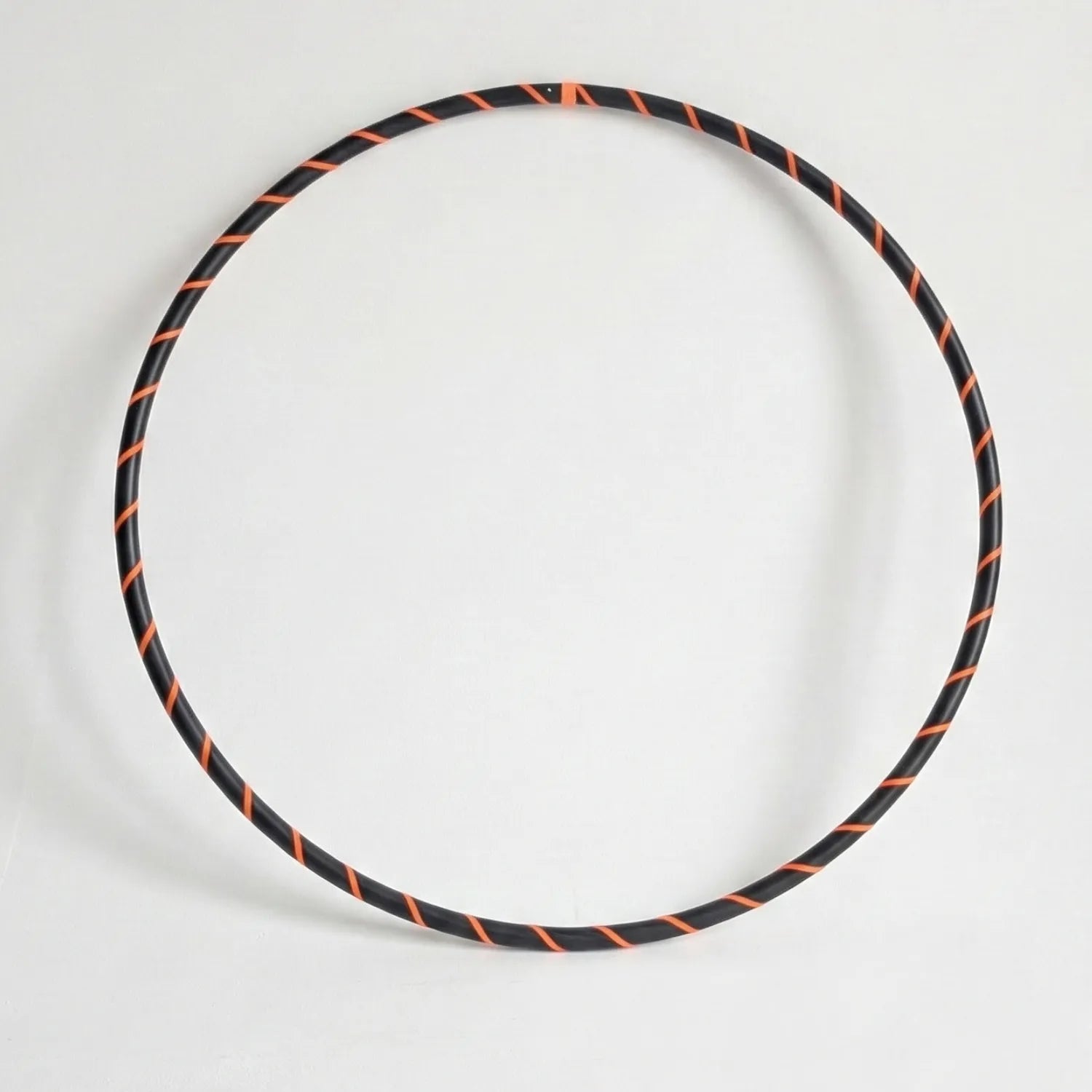 Studio shot of the B108 DESIGN weighted fitness hula hoop in obsidian black with a fluoro orange spiral grip tape pattern against a clean white backdrop.
