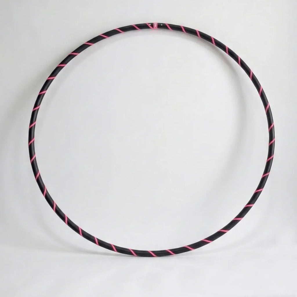 Studio shot of the B108 DESIGN weighted fitness hula hoop in obsidian black with a fluoro pink spiral grip tape pattern against a clean white backdrop.