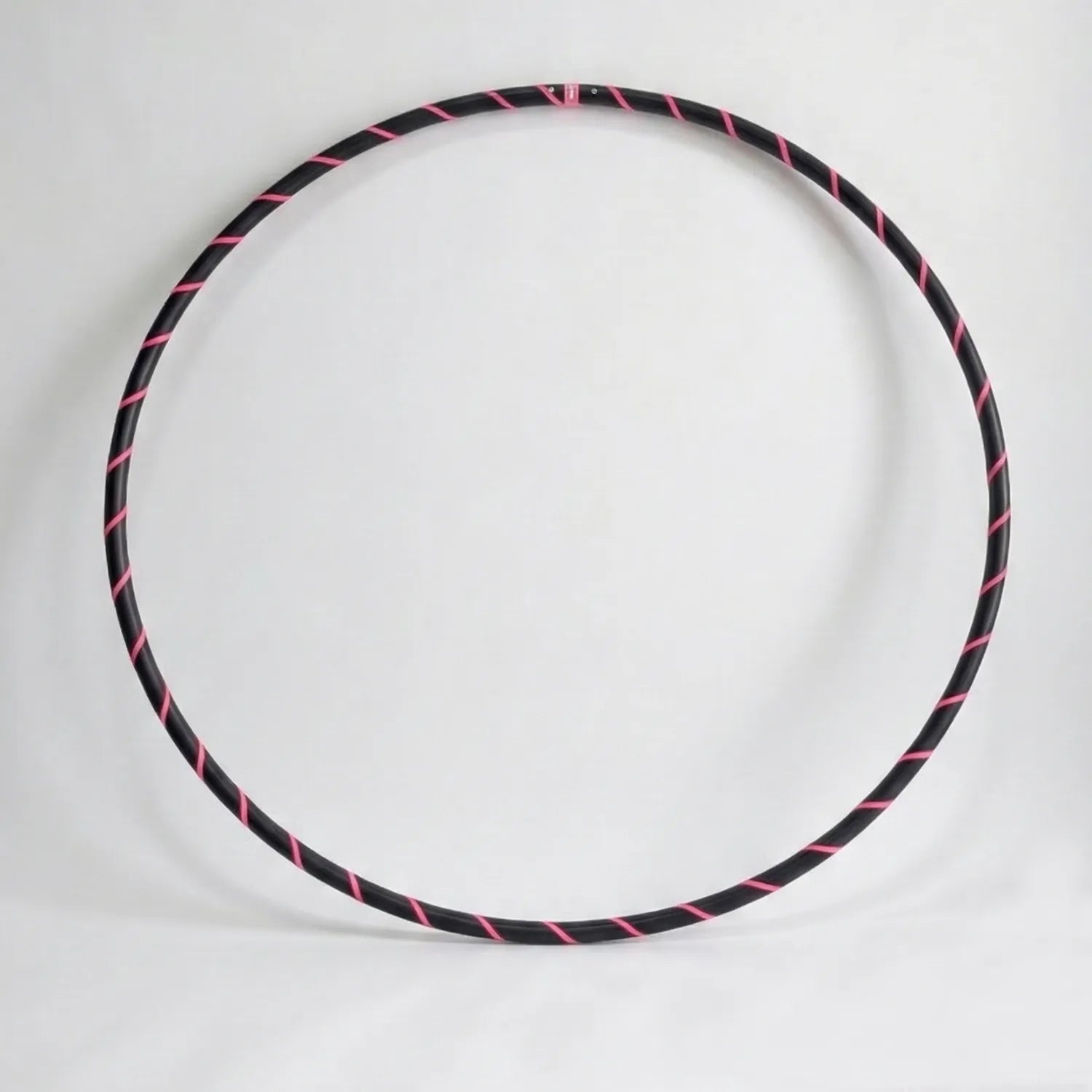 Studio shot of the B108 DESIGN weighted fitness hula hoop in obsidian black with a fluoro pink spiral grip tape pattern against a clean white backdrop.