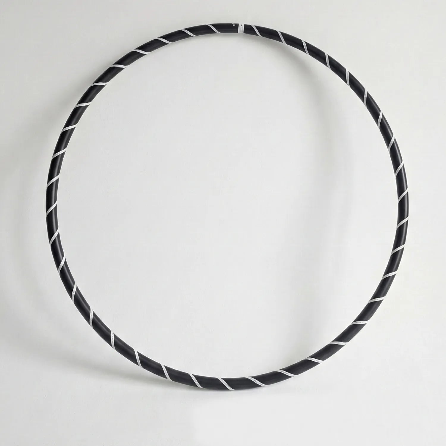 Studio shot of the B108 DESIGN weighted fitness hula hoop in obsidian black with a white spiral grip tape pattern against a clean white backdrop.